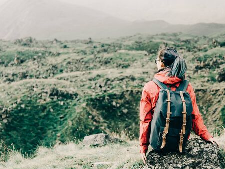 Explorer backpacker young woman resting on rocky stone outdoor, rear view.の写真素材