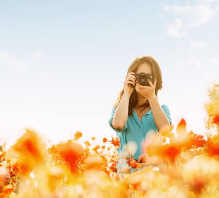 Girl photographing with a camera in flower meadow in summer outdoor.