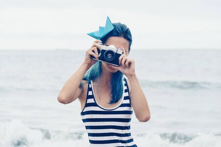 Beautiful young woman takes a photograph with old photo camera on beach in summerの写真素材