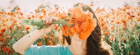 Unrecognizable young woman covered her face with bouquet of red poppies flowers in summer outdoor.の写真素材