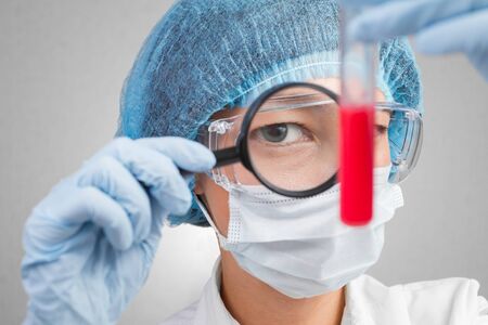 Female laboratory technician examines a test tube with the medium under a magnifying glassの写真素材