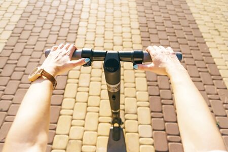 Unrecognizable young woman riding an electric scooter in street outdoor, point of view in first person. Concept of ecological transport.の写真素材