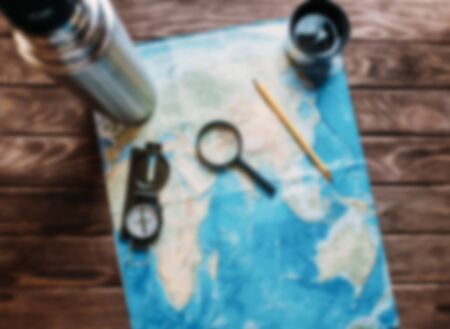 Map with a magnifying glass and compass on wooden background, top view. Concept of travel. Image with blurred effect.の写真素材