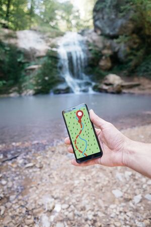 Explorer man using smartphone with GPS app outdoor. Male hiker trekking final location pin at waterfall. Point of view in first person.の写真素材