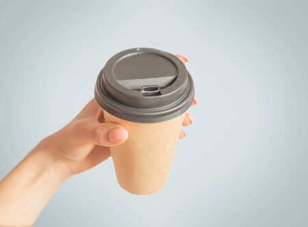 Female hand holding take away paper cup of coffee on a grey background, point of view in first person.の写真素材