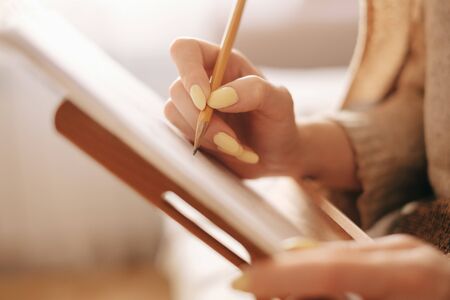 Close-up of female artist hand drawing a sketch on paper easel with pencil at home.の写真素材