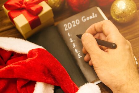 View of male hand writing checklist of 2020 goals in notebook on wooden table near New Year decorations, point of view.の写真素材