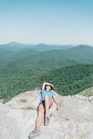 Explorer young woman resting on peak of rock high in summer mountains.の写真素材