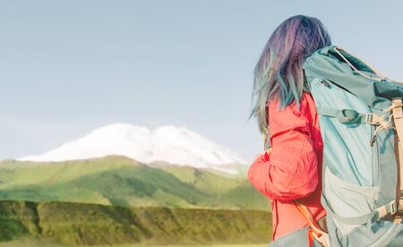 Unrecognizable hiker young woman with backpack looking at mountain Elbrus in summer outdoor.の写真素材