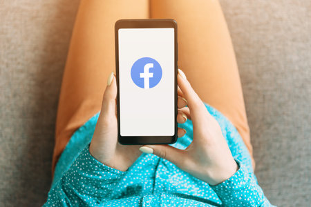 Gelendzhik, Russia, 19 November 2019: Unrecognizable young woman using Facebook App on her smartphone indoor. Point of view in first person.のeditorial素材