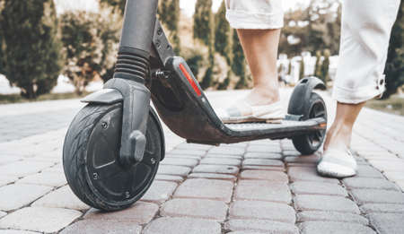 Unrecognizable young woman standing with electric scooter in street in summer, view of legs.の写真素材