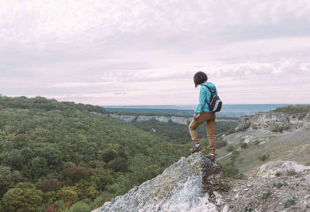 Lonely young traveler girl stands on stone at top of mountain. The traveler discovers new places.