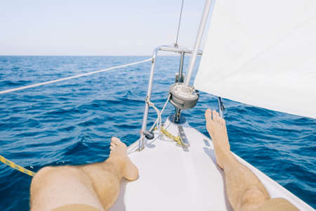 Unrecognizable young man resting on bow of yacht sailing in blue sea on sunny summer day, view of...