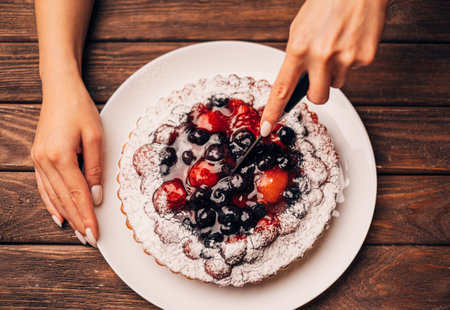 A woman cuts a berry pie into pieces. Close-up on hands with a knife. Top view.