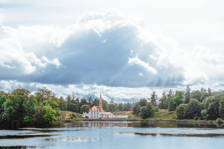 Gatchina, Saint-Petersburg, Russia, 25 August 2020: Priory palace by the Black lake in summer on background of epic cloudy sky. The sun's rays shine through the clouds on the historic building.のeditorial素材
