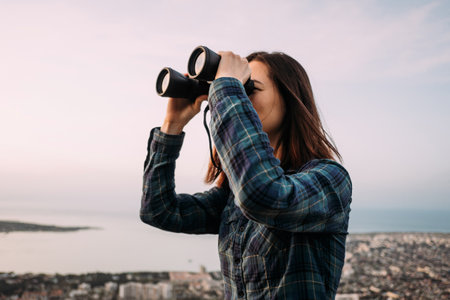 Portrait of a young female tourist looking through binoculars at sunset.の写真素材