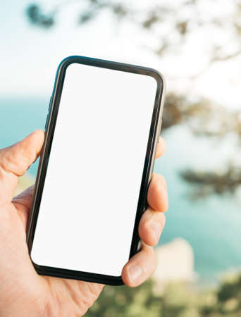 Man holds a cell phone in his hand against the backdrop of a natural sea landscape.の写真素材