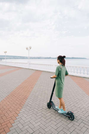 Young woman in a dress drives an electro scooter.