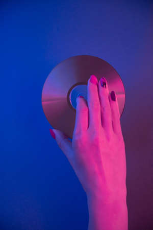 Female hand holds a compact disc on a blue background in purple neon light.の写真素材
