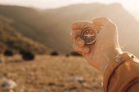 Compass in the hands of a tourist in the mountains during sunset.