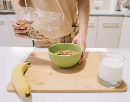 young woman pours granola into a plate for breakfast.