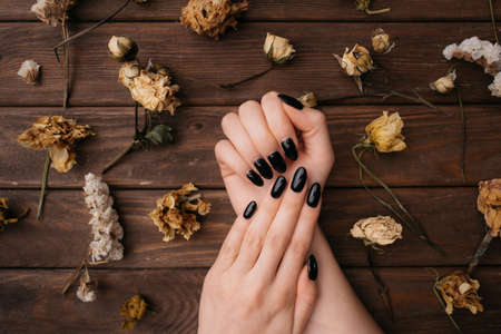 Female hands with black manicure among dry flowers on a wooden background.の写真素材