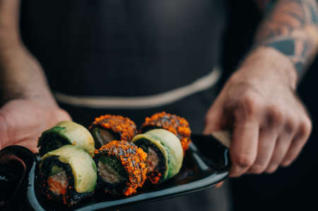 Unrecognizable male chef holds black rice sushi rolls on a cutting board.の写真素材