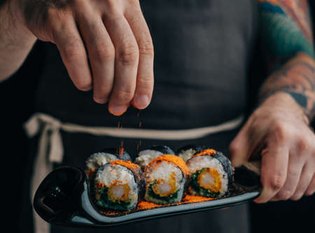 Man sprinkles spices on sushi rolls to serve the dish.の写真素材