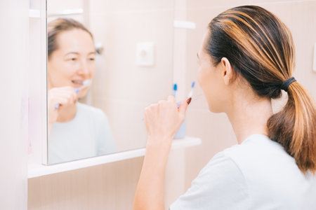 Woman with braces cleans her teeth with a toothbrush, before mirror. Selective focus on the person.の写真素材