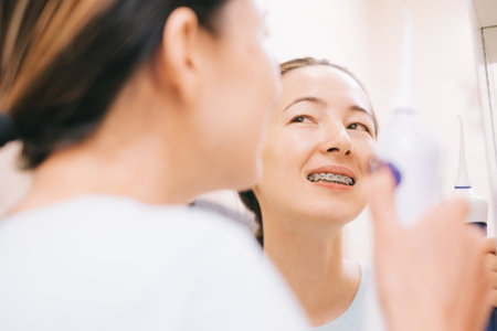 Young woman with braces looks in the mirror after brushing her teeth.の写真素材