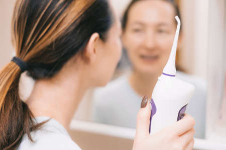 A woman with braces looks in the mirror. Selective focus on oral irrigator in hand.の写真素材