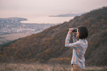 Young woman in the mountains looks through binoculars.の写真素材