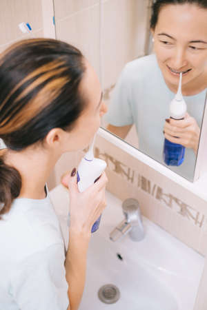 Young woman brushing teeth with braces using an oral irrigator.の写真素材