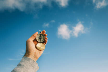 Vintage compass in the hands of the traveler against the blue sky.の写真素材