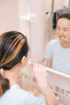 Young woman with braces cleans her teeth with a special dental brush, before mirror. Selective focus on the person.の写真素材