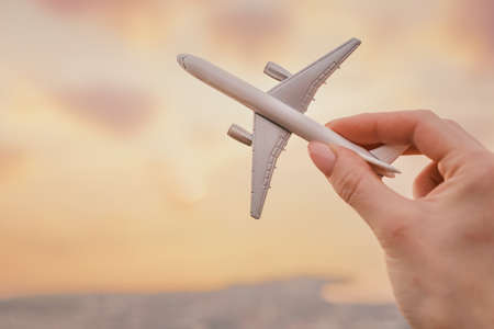 Woman holds an airplane model in her hand in the background sky during sunset. Close-up view.の写真素材