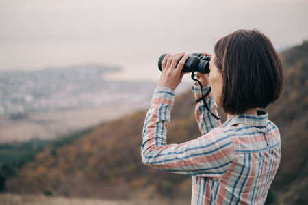 Young woman looks through binoculars and admires the mountain scenery.の写真素材