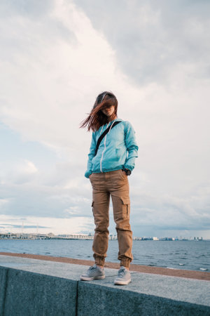 A full-length portrait of a young woman in a blue windbreaker in windy weather.の写真素材