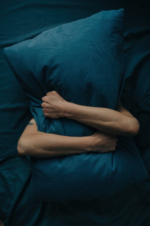A young unrecognizable woman hides under a pillow. The woman presses the pillow tightly against her face.の写真素材