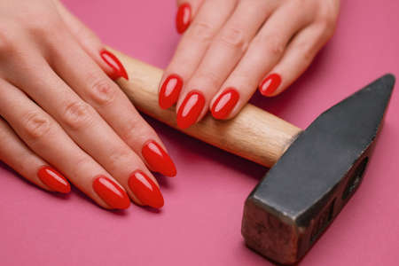 Close-up of a womans hand with a red manicure and a hammer.の写真素材