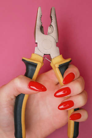 Womans hand with red nails holding pliers.の写真素材