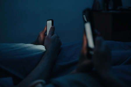 A man and a woman lie in pastels at night and use their phones. Checking social media before bed.の写真素材