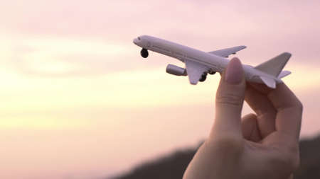 Airplane model in a female hand in the background sky during sunset.の写真素材