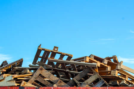 Garbage removal. A large pile of used wooden pallets lies in a metal trash container in random...