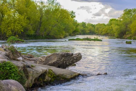 Image of a very large river with green trees on the shore and clouds in the backgroundの写真素材