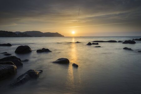 Sunrise over the horizon of a beach with rocks in the middle of the beach