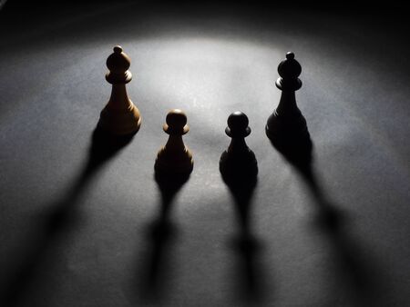 Image of two bishops a black and a white and two pawns a black and a white backlighting with black backgroundの写真素材