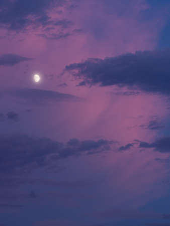 Vertical photo of the moon lit with very intense blue and pink clouds