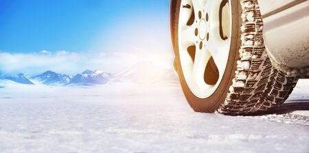 Wheel of a car on a white snowy surface close-up against a background of mountains. Space for text