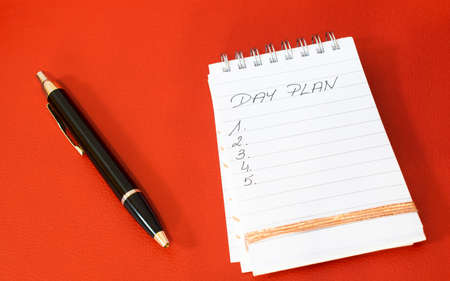 plan of the day notebook and pen on a red background
